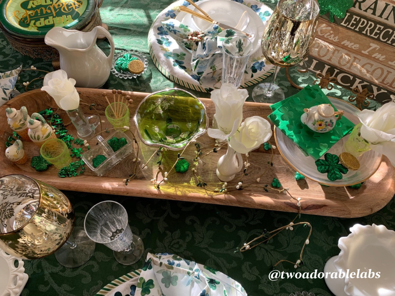 This tablescape is a combination of new and vintage pieces with a St. Patrick’s Day and easy access to everything kinda table.  Have you ever sat down at a table and can’t find the salt, pepper, oil, vinegar, and are in need of a toothpick at the end of your meal?  Well, this table has it all right in the middle.  I used a bread bowl from TJMaxx and filled it with a antique vinegar and oil set, antique shot glasses to hold tooth picks, antique salt and pepper shakers, antique vases to hold silk flowers for height and color and of course, some napkins and sparkly lucky charms from Dollar General.  